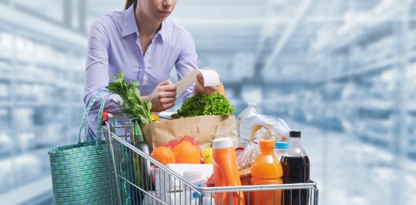 Woman pushing a cart and checking a grocery receipt, grocery shopping and expenses concept